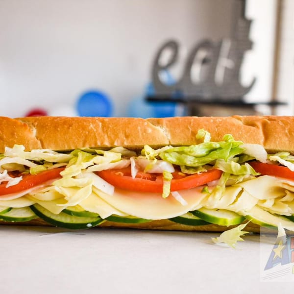A large All American Heroes sandwich filled with cheese, tomatoes, cucumbers, and lettuce.