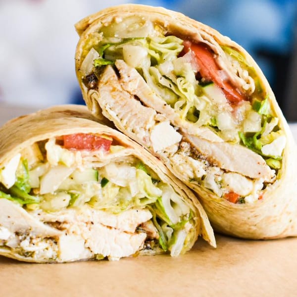 Two halves of a chicken wrap, filled with lettuce, tomatoes, and feta cheese.