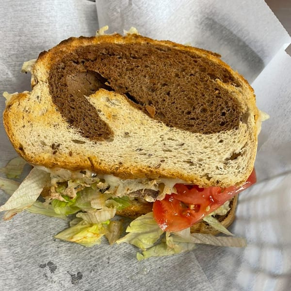 A close-up of an All American Heroes sandwich with marbled rye bread, lettuce, and tomato.